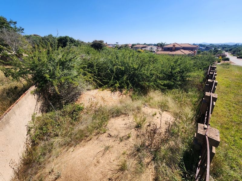 An elevated view of a vacant residential plot featuring overgrown vegetation, boundary walls, and perimeter fencing in a suburban neighborhood setting.