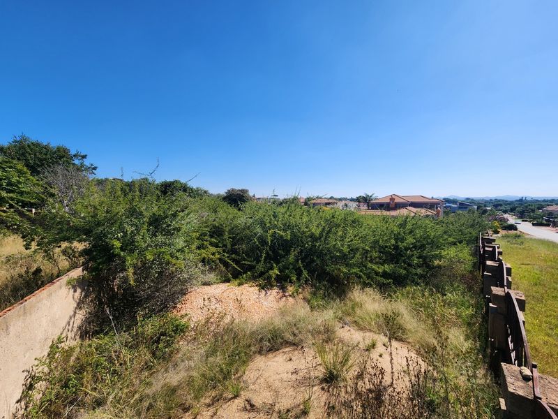 A vacant residential plot featuring overgrown vegetation, boundary walling, and fencing, situated in a developed neighborhood setting.