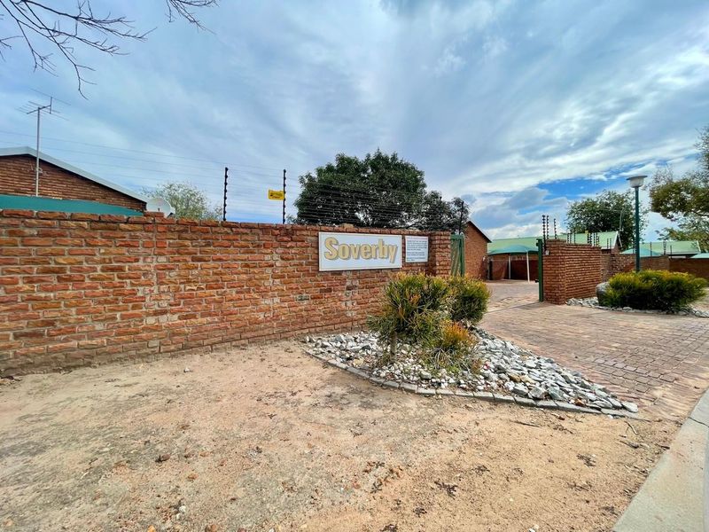 Front entrance view of the Soverby complex, featuring a brick boundary wall, electric fencing, and a paved driveway entrance.