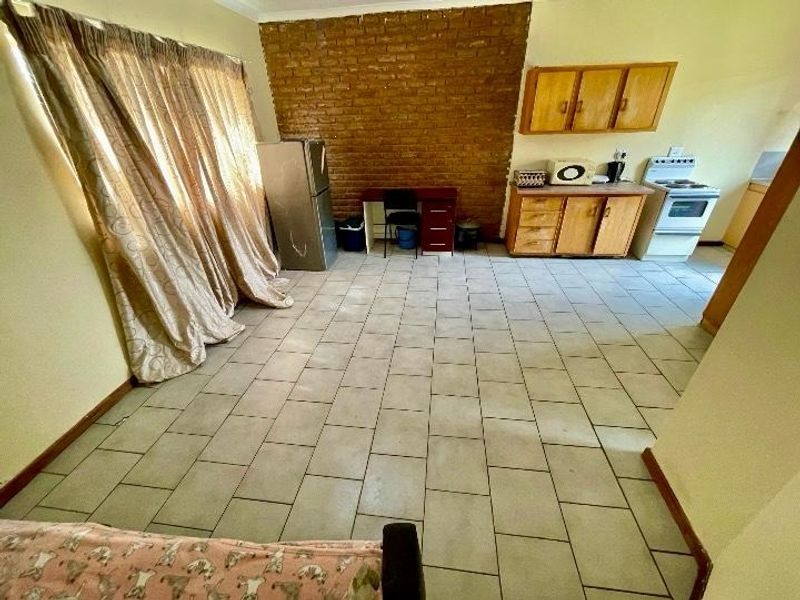 Open-plan living and kitchen area featuring tiled flooring, an exposed brick feature wall, and functional kitchen cabinetry with a freestanding stove.