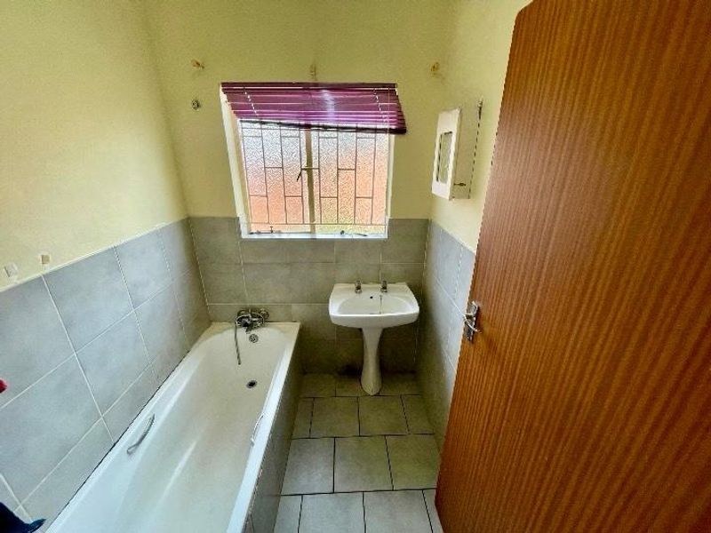 A functional bathroom featuring a pedestal basin, bathtub, and tiled finishes, requiring minor cosmetic updates to enhance its overall appeal.