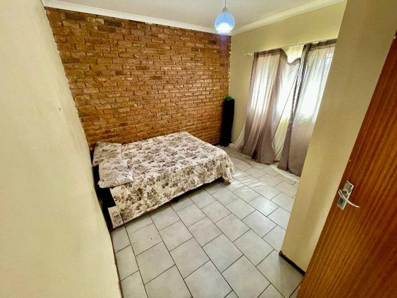 A bedroom featuring an exposed brick accent wall, neutral tiled flooring, and a coved ceiling, offering a solid foundation for modern interior updates.