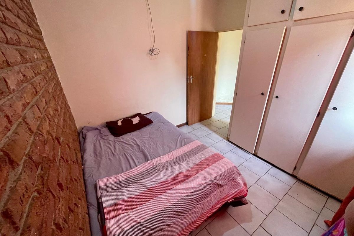 A bedroom featuring tiled flooring, built-in cupboards, and an exposed brick feature wall, requiring minor cosmetic updates and electrical finishing.