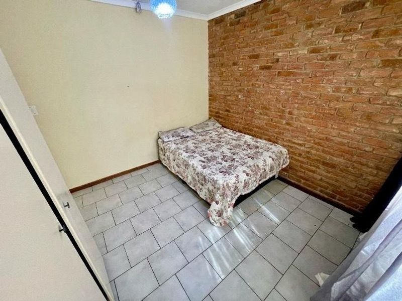 A bedroom featuring an exposed brick feature wall and tiled flooring, offering a rustic aesthetic with potential for modern updates.