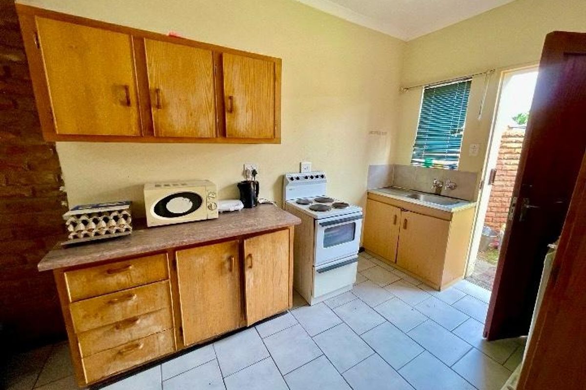 A functional kitchen featuring wooden cabinetry, laminate countertops, a freestanding electric stove, and tiled flooring with direct access to the exterior.