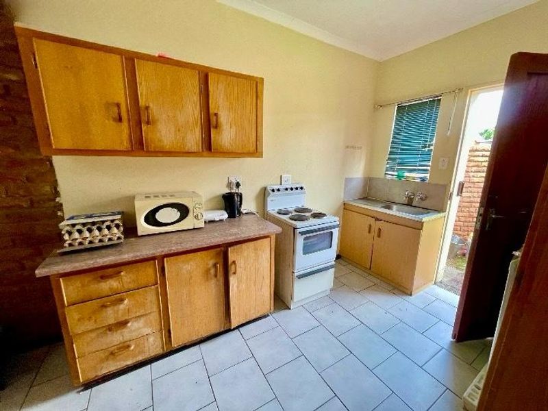A functional kitchen featuring wooden cabinetry, laminate countertops, a freestanding electric stove, and tiled flooring with direct access to the exterior.