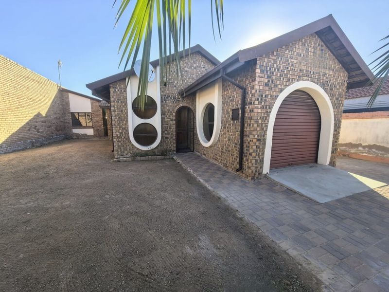 Front view of a face brick house featuring a single roll-up garage, arched window detailing, and a paved driveway with an unlandscaped front yard.