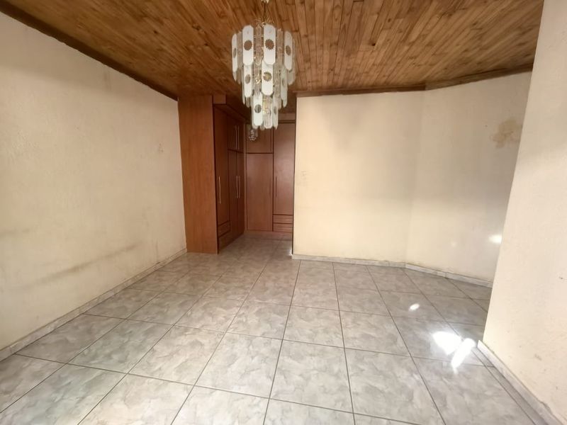 An empty bedroom featuring tiled flooring, a wooden ceiling, and built-in wooden cupboards.