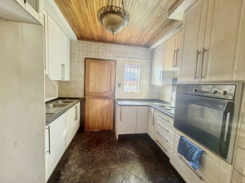 A functional kitchen featuring built-in cabinetry, a double sink, integrated oven, tiled backsplash, and a distinctive timber-paneled ceiling.