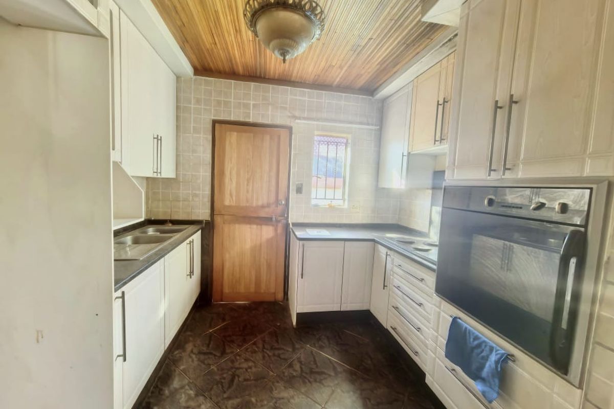 A functional kitchen featuring built-in cabinetry, a double sink, integrated oven, tiled backsplash, and a distinctive timber-paneled ceiling.