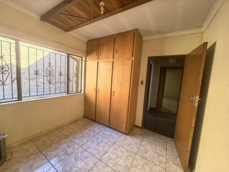 A vacant bedroom featuring tiled flooring, built-in wooden cupboards, and a decorative wooden ceiling panel with security bars on the window.