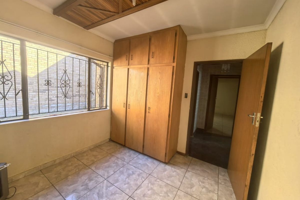 A vacant bedroom featuring tiled flooring, built-in wooden cupboards, and a decorative wooden ceiling panel with security bars on the window.