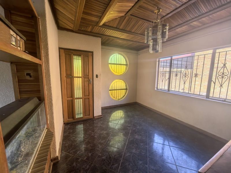 A living area featuring a unique timber-clad ceiling, circular windows with security bars, and dark tiled flooring, offering a dated but functional space.