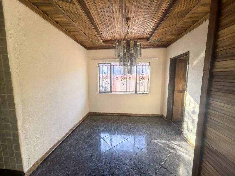 An empty dining room featuring a distinctive timber-clad tray ceiling, tiled flooring, and a window fitted with security bars.