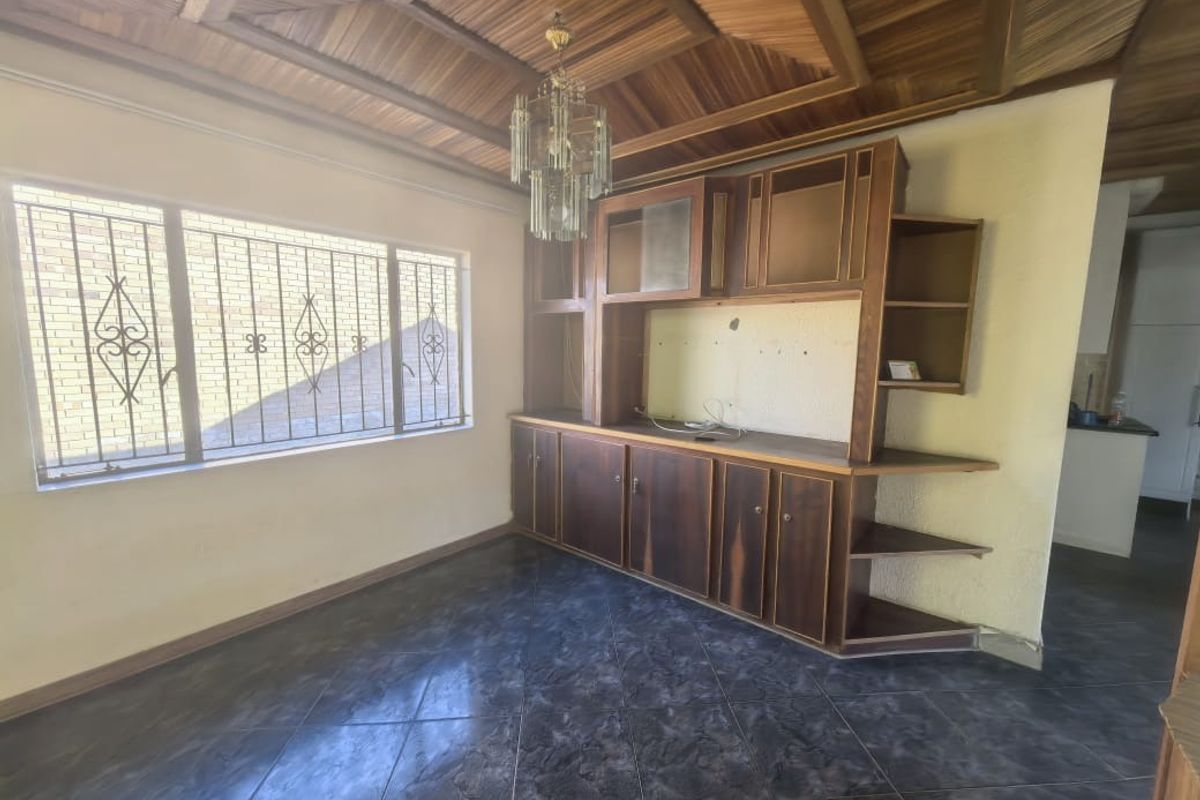Living area featuring a distinctive timber-clad vaulted ceiling, built-in wooden cabinetry, tiled flooring, and security bars on the windows.