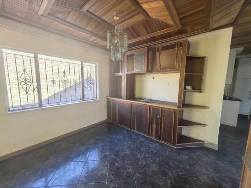 Living area featuring a distinctive timber-clad vaulted ceiling, built-in wooden cabinetry, tiled flooring, and security bars on the windows.