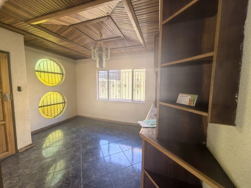 A living area featuring a distinctive timber-clad ceiling, circular windows with security bars, and built-in wooden shelving, finished with dark floor tiles.