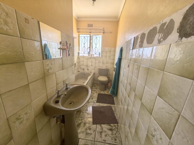 A dated bathroom featuring a pedestal basin, bathtub, and toilet, with partially tiled walls requiring repair and modernization.