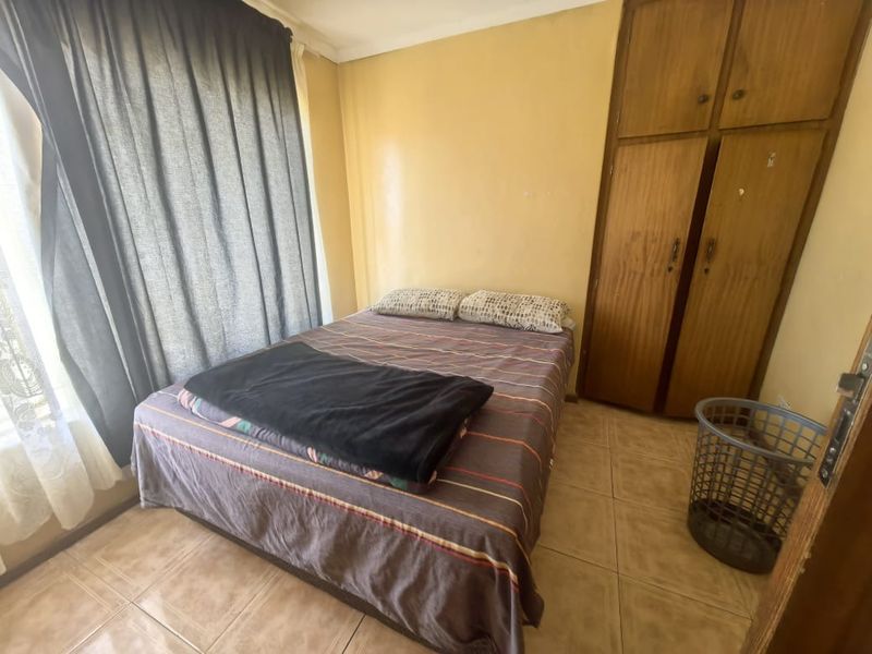 A compact bedroom featuring tiled flooring and a built-in wooden wardrobe, offering a functional space with potential for cosmetic updates.