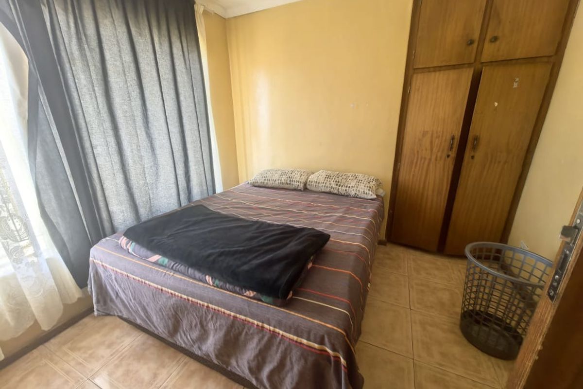 A compact bedroom featuring tiled flooring and a built-in wooden wardrobe, offering a functional space with potential for cosmetic updates.