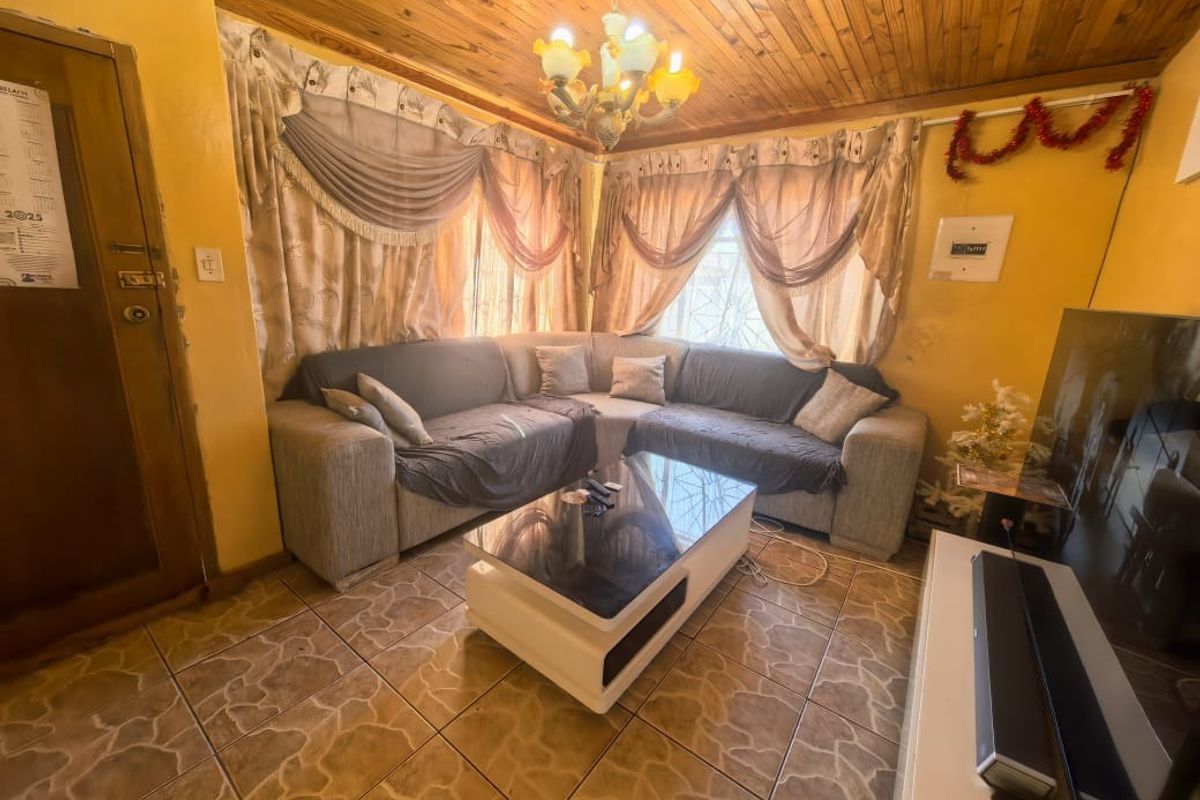 A living room featuring ceramic floor tiles and a timber tongue and groove ceiling, providing a dated aesthetic that could benefit from modernization.