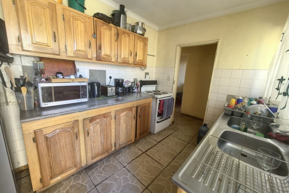 A functional kitchen featuring wooden cabinetry, laminate countertops, a double stainless steel sink, and a freestanding stove, offering potential for modernization.