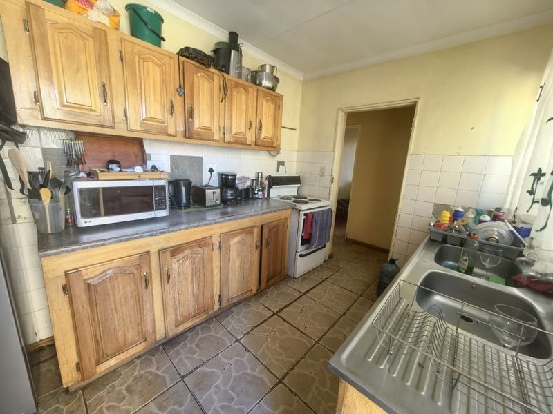 A functional kitchen featuring wooden cabinetry, laminate countertops, a double stainless steel sink, and a freestanding stove, offering potential for modernization.