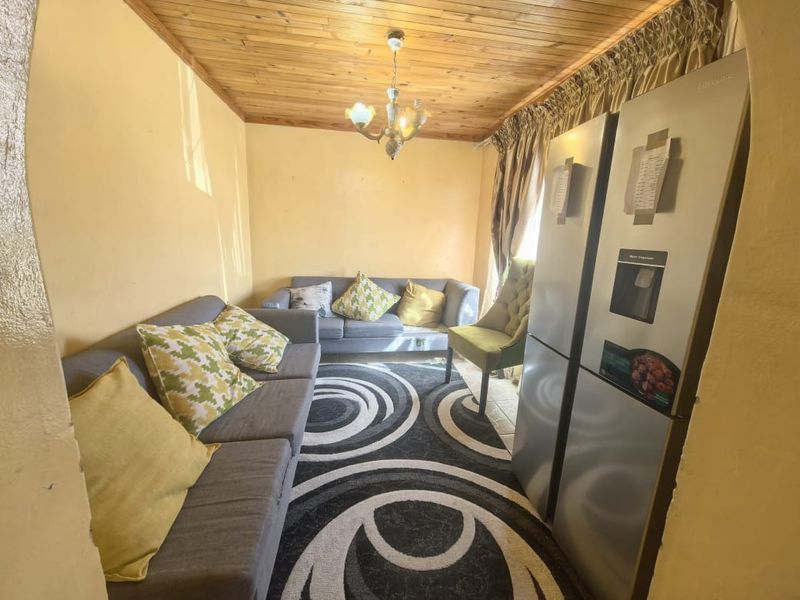 A compact living area featuring a timber tongue and groove ceiling and an arched entryway, offering a cozy space with potential for modernization.