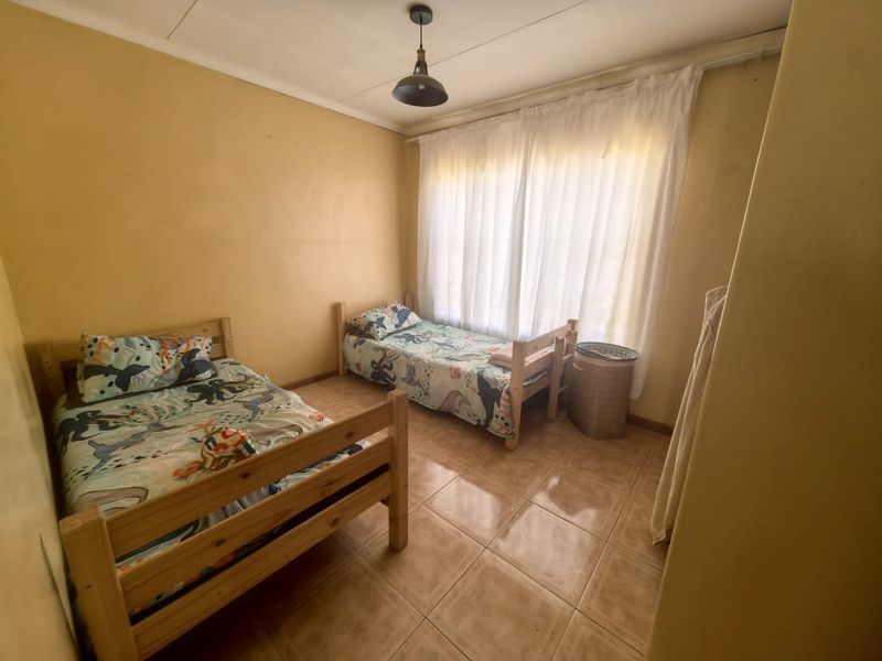 A functional bedroom featuring tiled flooring and a large window with curtains, providing a blank canvas for potential cosmetic updates.