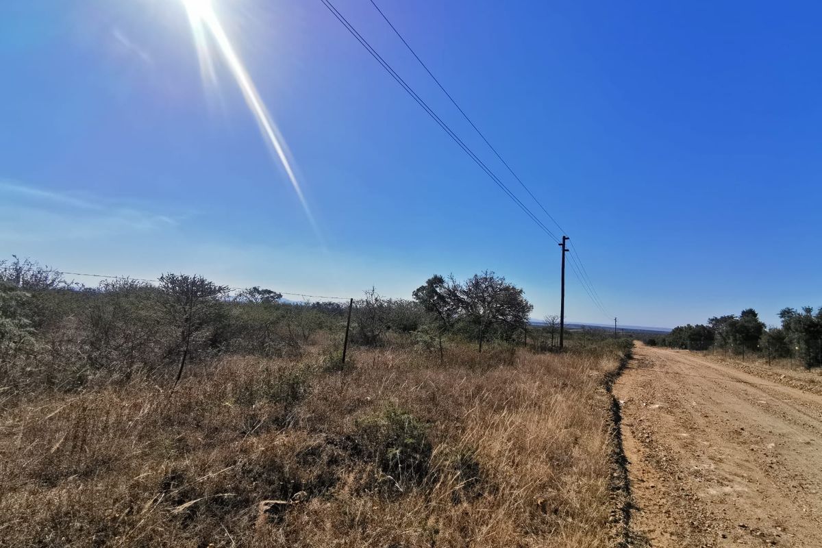 A view of a dirt road bordering a vacant residential plot, featuring overhead power lines and existing wire fencing.