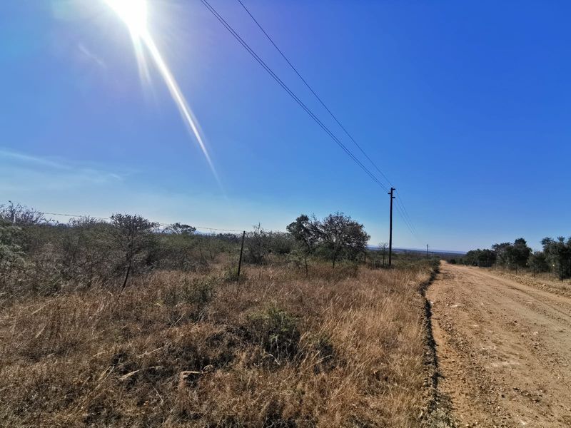 A view of a dirt road bordering a vacant residential plot, featuring overhead power lines and existing wire fencing.