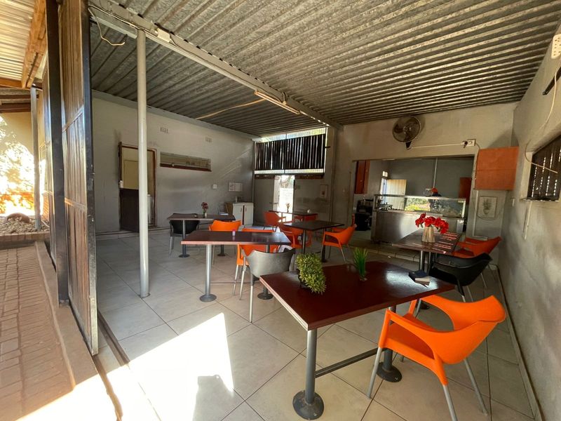 A spacious covered patio area featuring tiled flooring and a corrugated metal roof, suitable for outdoor dining or entertainment.