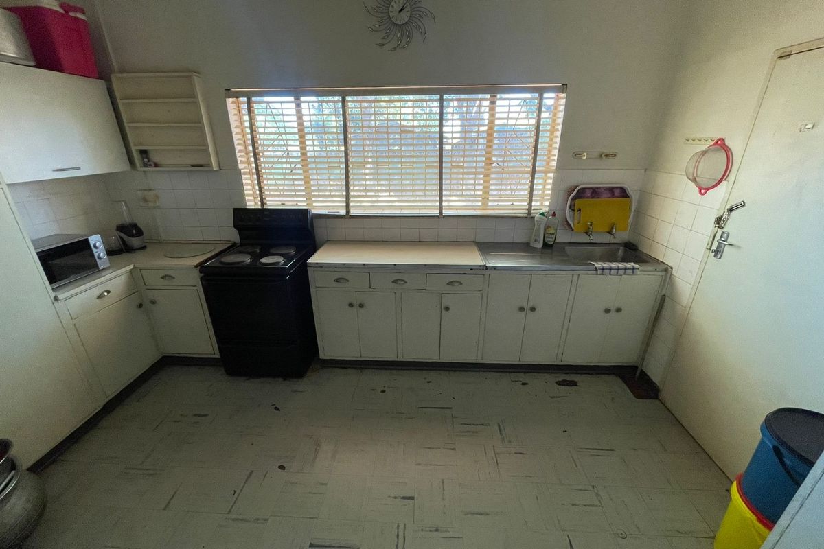 A functional kitchen featuring original cabinetry, a stainless steel sink, tiled backsplash, and a freestanding stove, offering potential for modern renovation.