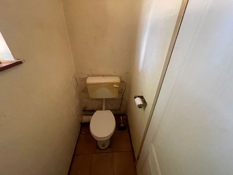 A small, dated guest toilet featuring tiled flooring and walls in need of cosmetic repair and refurbishment.