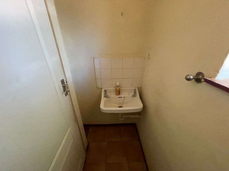 A small, functional cloakroom or powder room featuring a wall-mounted basin with a tiled splashback and tiled flooring.