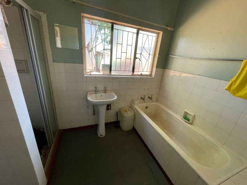 A dated bathroom featuring a pedestal basin, built-in bathtub, and shower enclosure, requiring renovation to update the finishes and fixtures.