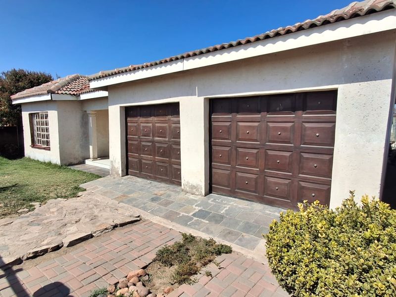 Front view of a house featuring a double garage with wooden doors, a tiled roof, and a paved driveway area.