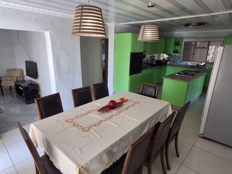 Open-plan kitchen and dining area featuring bright green cabinetry, a central island with a cooktop, and tiled flooring throughout.