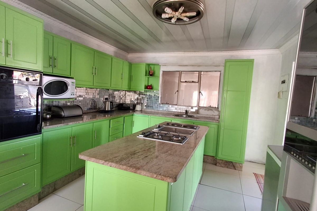 Kitchen featuring bright green cabinetry, granite countertops, a central island with a gas hob, built-in oven, and tiled flooring.