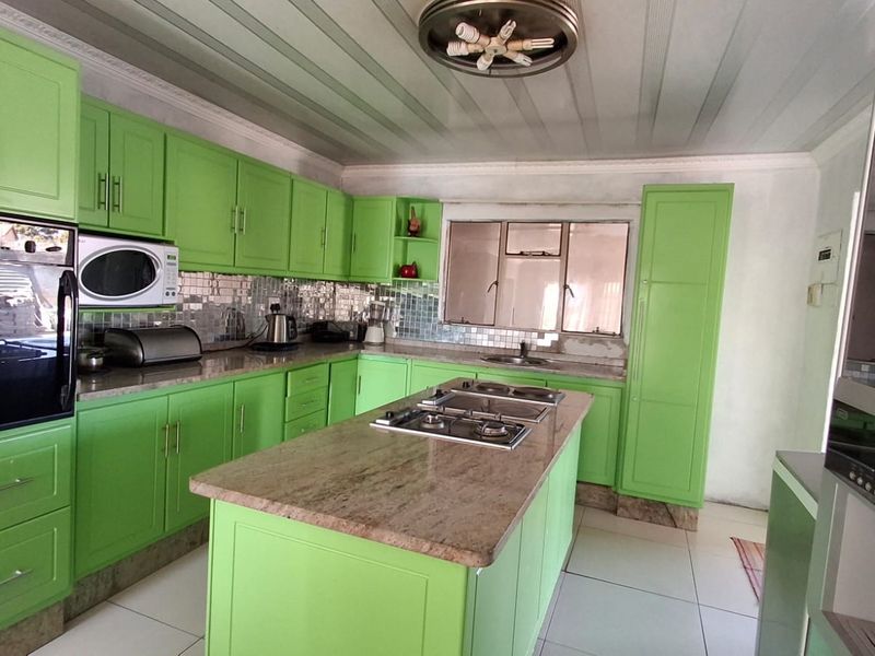 Kitchen featuring bright green cabinetry, granite countertops, a central island with a gas hob, built-in oven, and tiled flooring.
