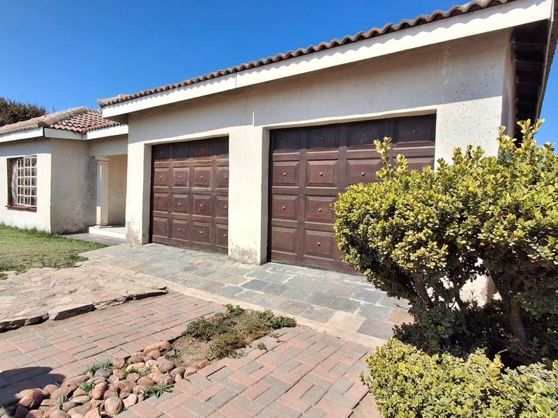 Front elevation of a residential property featuring a double garage with timber doors, tiled roof, and paved driveway area.