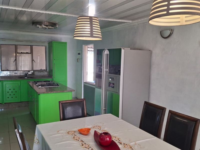 Open plan kitchen and dining area featuring vibrant green cabinetry, a central island with a built-in hob, and tiled flooring throughout.