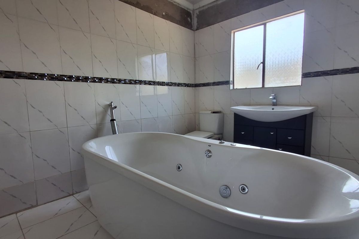 A bathroom featuring a freestanding jetted bathtub, vanity cabinet with basin, and toilet, with tiled finishes and visible unfinished wall sections near the ceiling.