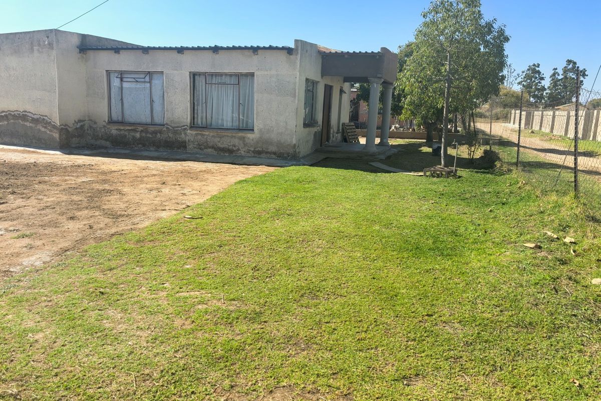 Rear view of a residential property featuring a covered patio area, concrete columns, and a large grassed yard enclosed by wire fencing.