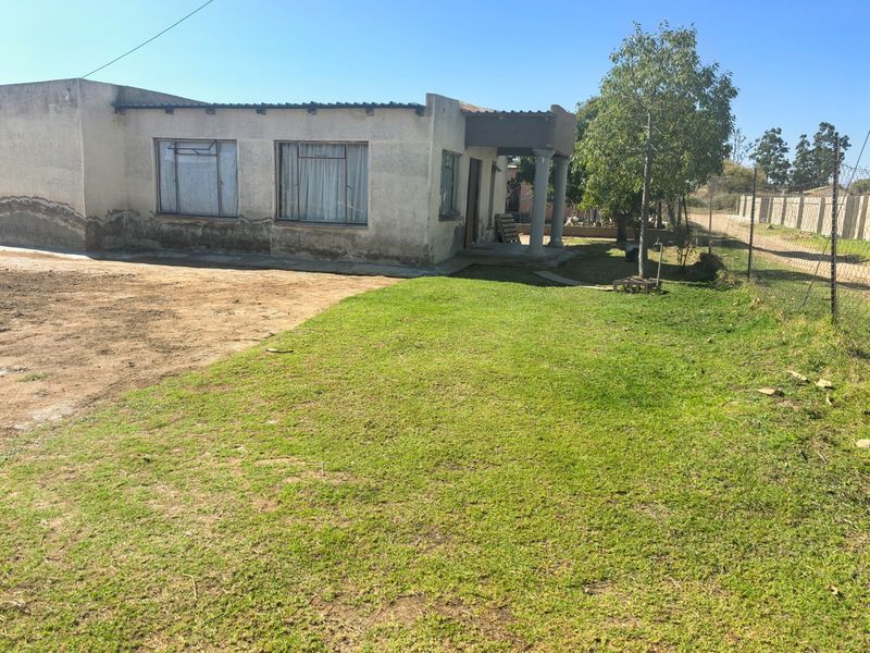 Rear view of a residential property featuring a covered patio area, concrete columns, and a large grassed yard enclosed by wire fencing.