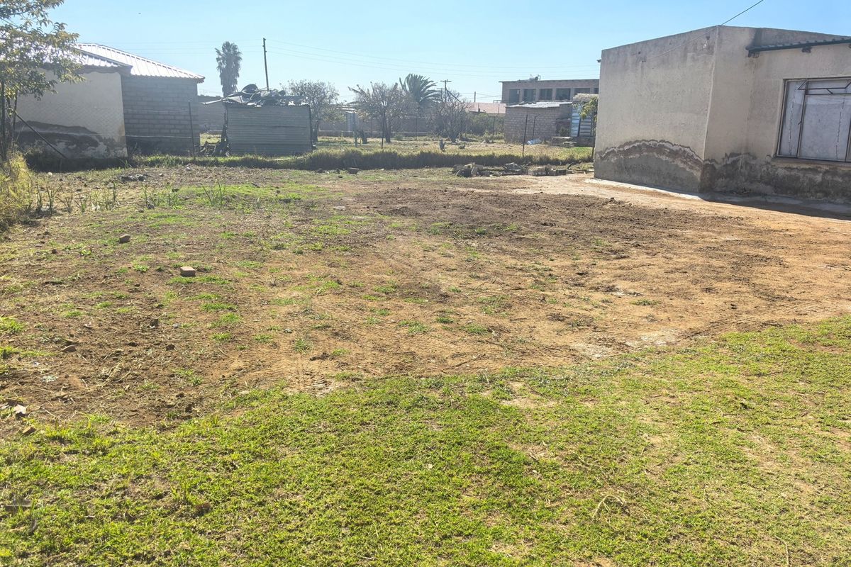 A view of the rear yard area showing open land and adjacent building structures with visible exterior wall deterioration.