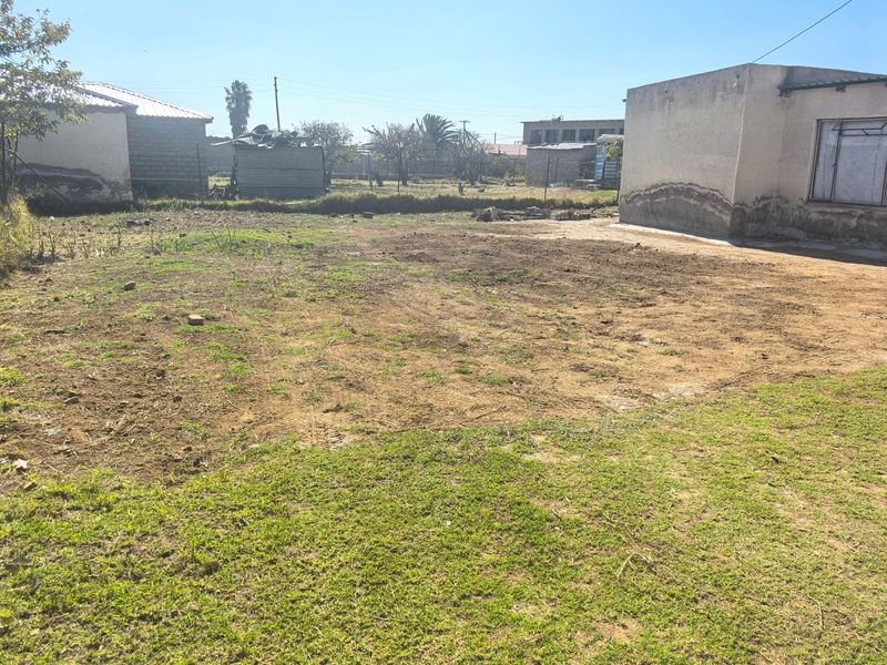 A view of the rear yard area showing open land and adjacent building structures with visible exterior wall deterioration.