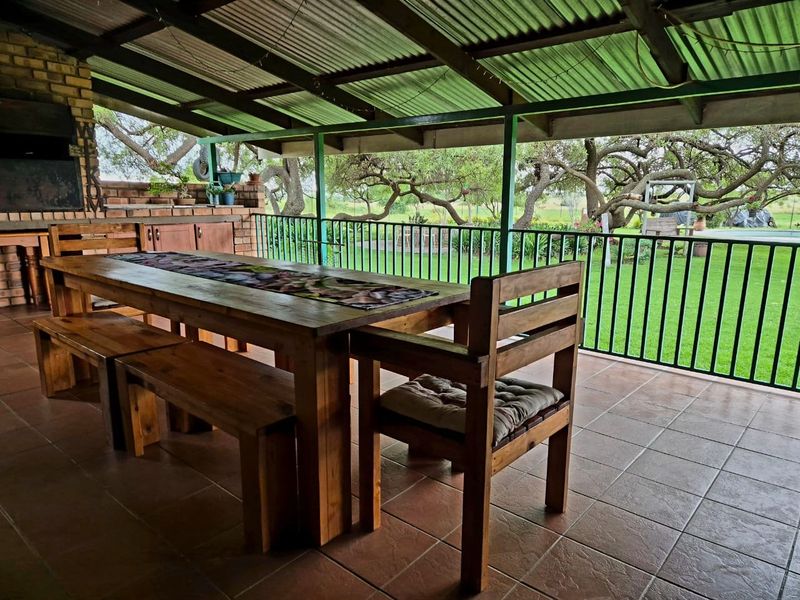Covered outdoor patio featuring a built-in braai, tiled flooring, and metal railings, overlooking a spacious garden area.