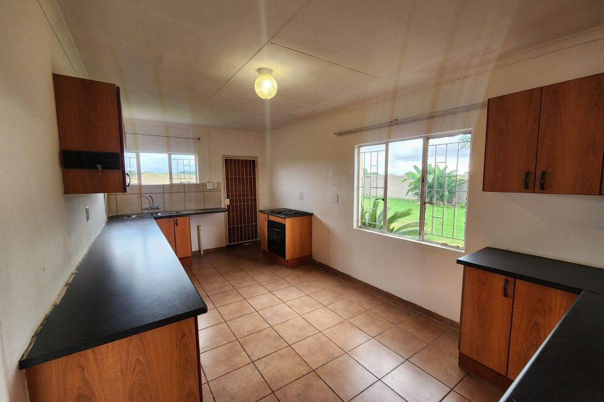 A functional kitchen featuring wooden cabinetry, laminate countertops, built-in oven and hob, tiled flooring, and large windows overlooking the garden.