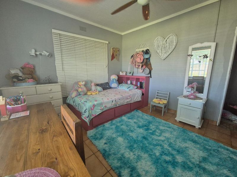 A functional bedroom featuring tiled flooring, a ceiling fan, and venetian blinds, offering a comfortable space with neutral wall finishes.